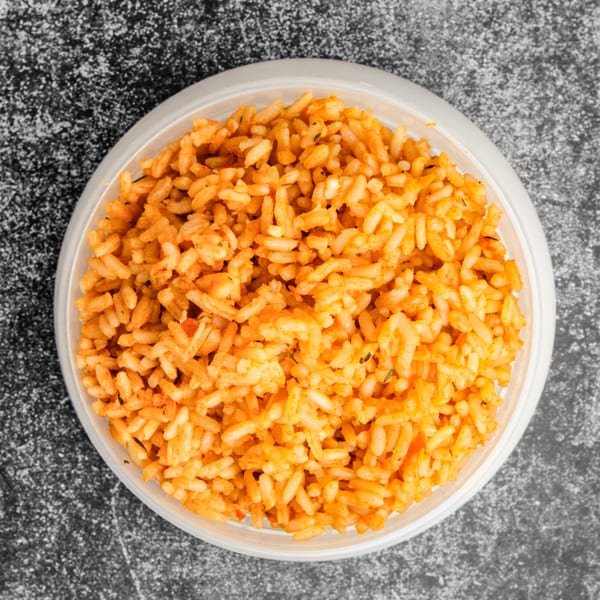 Overhead view of a white bowl filled with vibrant orange jollof rice from Suya Outpost.