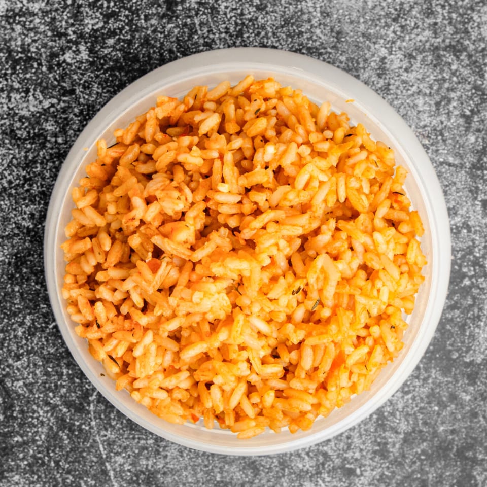 Overhead view of a white bowl filled with vibrant orange jollof rice from Suya Outpost.