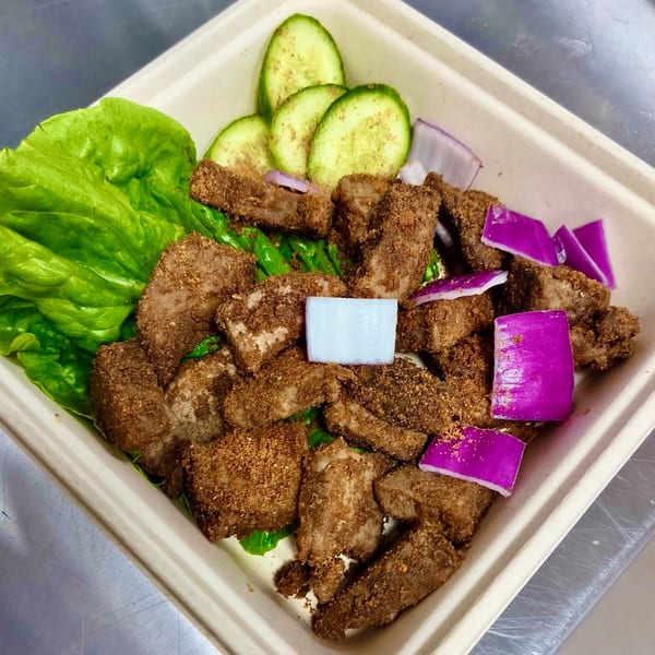 Suya Outpost's African-fusion dish with seasoned meat, lettuce, cucumber slices, and red onion in a takeout container.