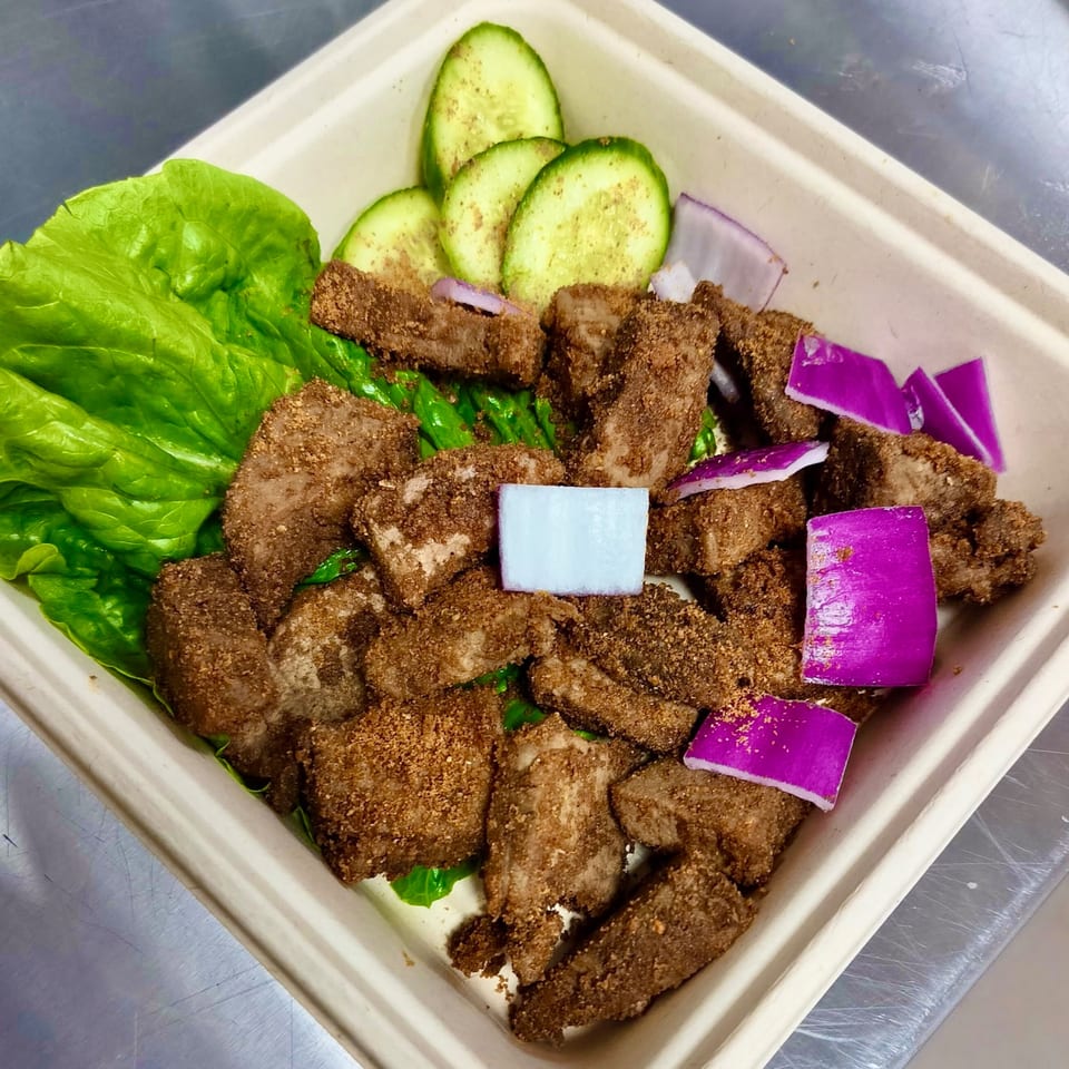 Suya Outpost's African-fusion dish with seasoned meat, lettuce, cucumber slices, and red onion in a takeout container.
