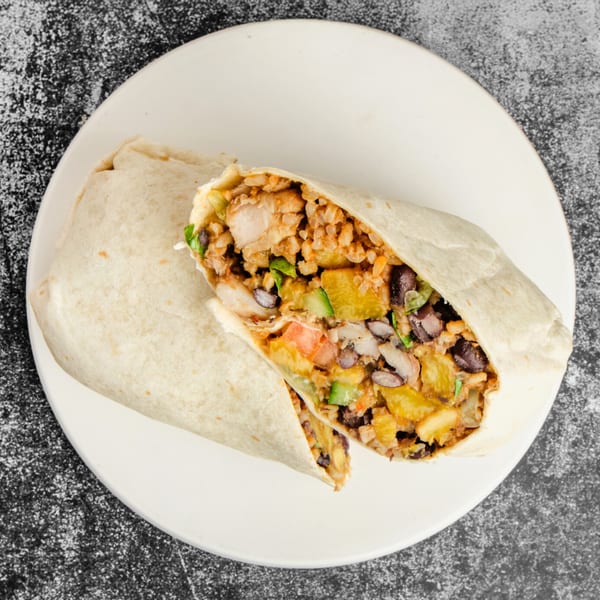 A Suya Outpost burrito, cut in half, filled with chicken, rice, black beans, and vegetables.