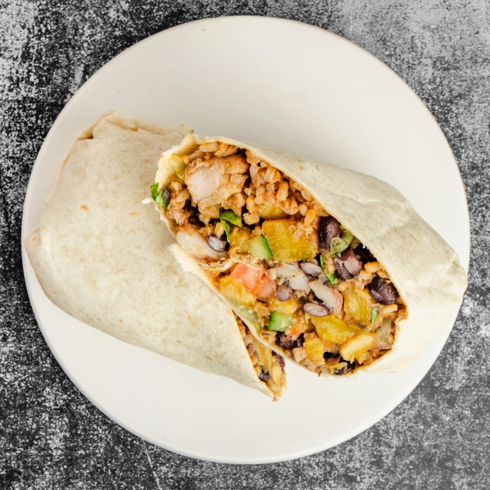 A Suya Outpost burrito, cut in half, filled with chicken, rice, black beans, and vegetables.