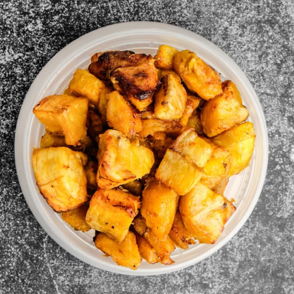 Overhead view of golden brown fried plantain chunks in a white plastic container.