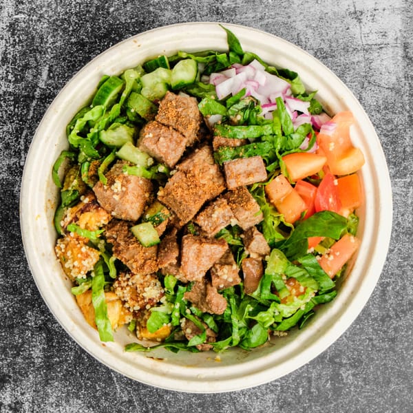 Suya Outpost's African-fusion salad bowl with seasoned meat, lettuce, cucumbers, red onions, and tomatoes.
