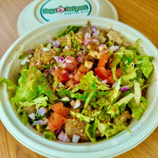 Suya Outpost Nigerian Grill bowl with lettuce, tomatoes, onions, and seasoned meat.